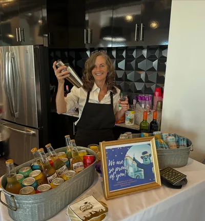 A bartender behind a drinks station at an event bar with glassware and service setup